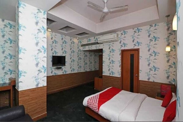 Une chambre d’hôtel avec un lit, un ventilateur de plafond, une télévision et un papier peint à motifs floraux.