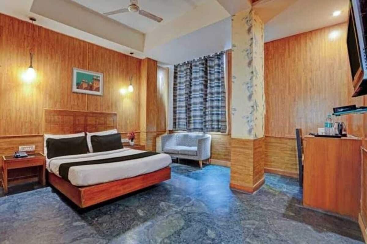 A hotel room with a wooden headboard, a bed, a desk, a chair, and a television.