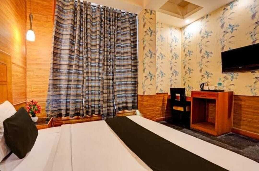 Una habitación de hotel con cama, escritorio, televisor y ventana con cortinas.