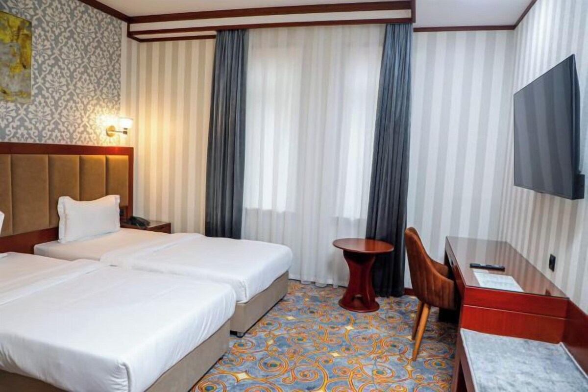 Ein Hotelzimmer mit zwei Betten, einem Schreibtisch, einem Stuhl, einem Fernseher und einem gemusterten Teppich.