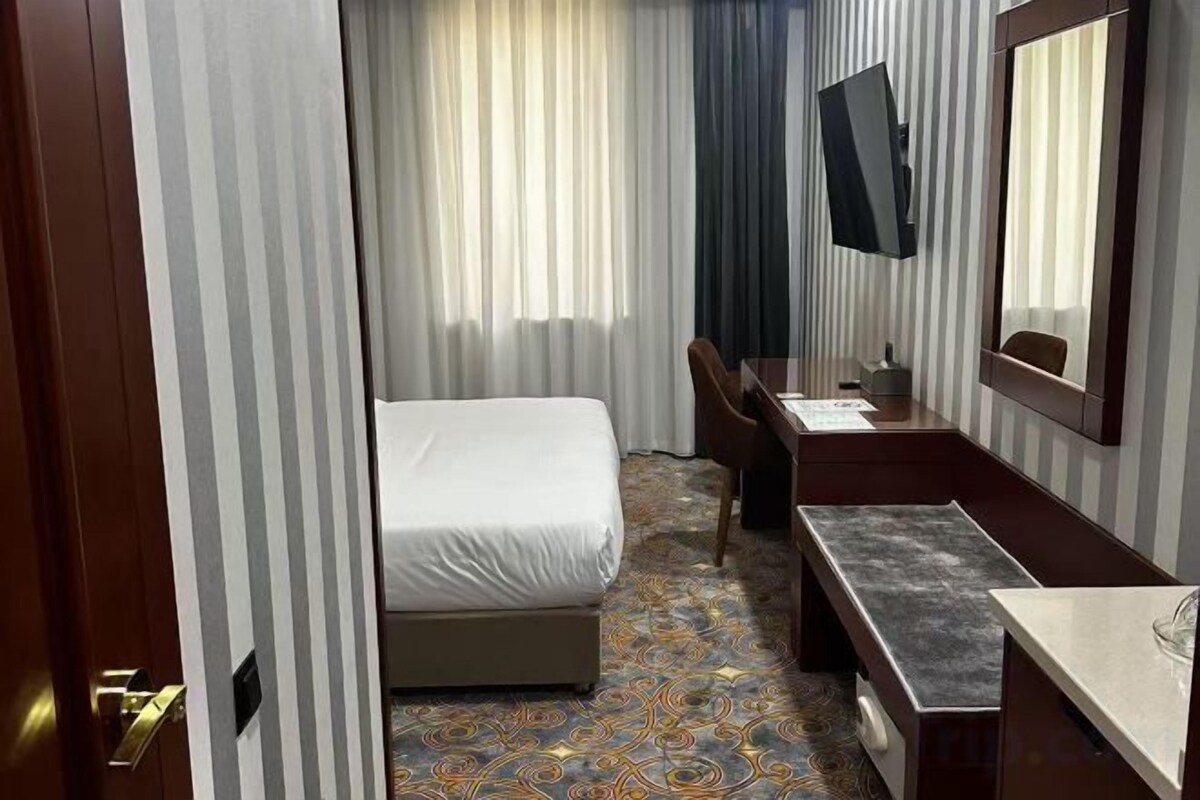 Ein Hotelzimmer mit Bett, Schreibtisch, Stuhl, Spiegel und einem Fenster mit Vorhängen.