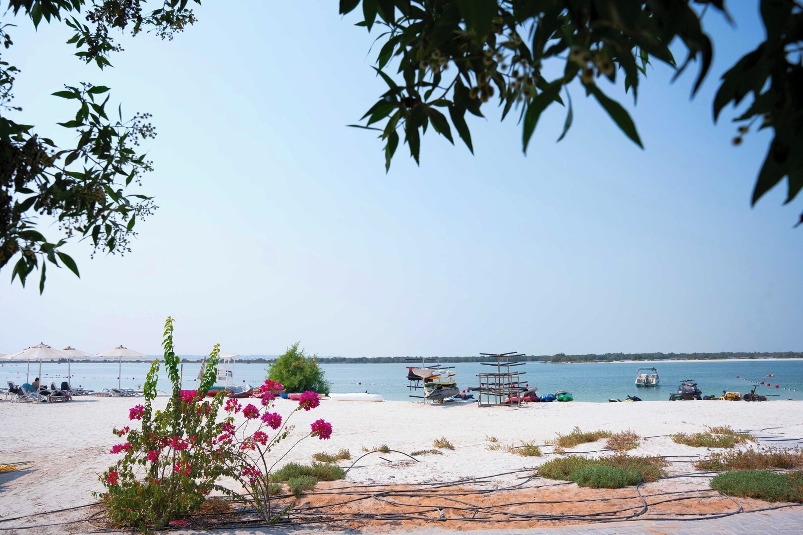 Ein Strand mit Sonnenschirmen, Booten und blauem Himmel.