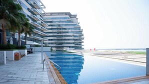 Ein modernes Hotel mit großem Infinity-Pool, Blick auf den Strand und einem mehrstöckigen Gebäude mit Balkonen.