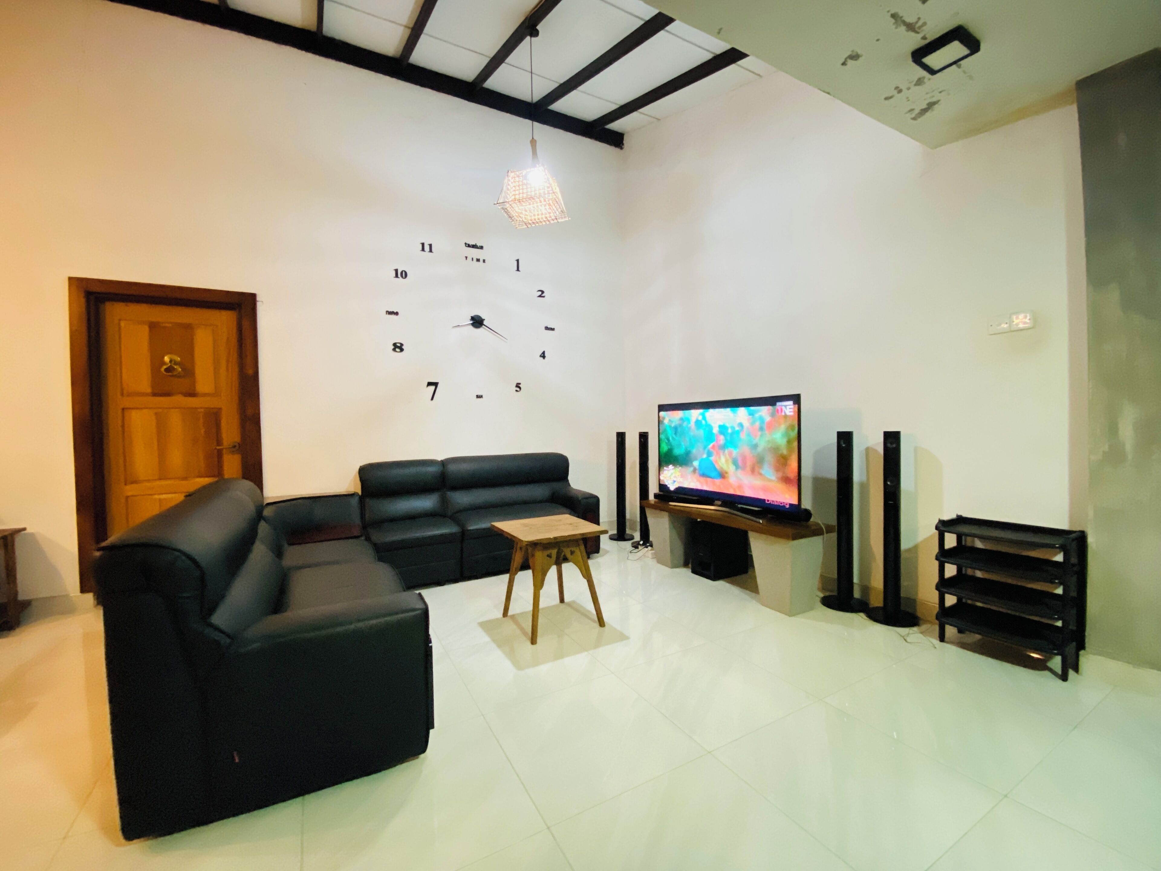 A living room with a black sofa, a wooden coffee table, a TV on a stand, and a wall clock.