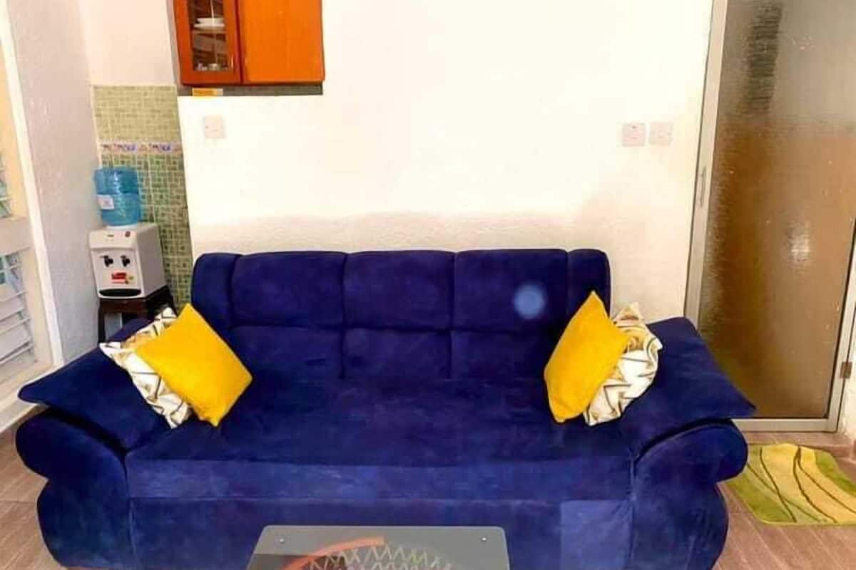 A dark blue sofa with yellow cushions in a room with a tiled wall and a water dispenser.