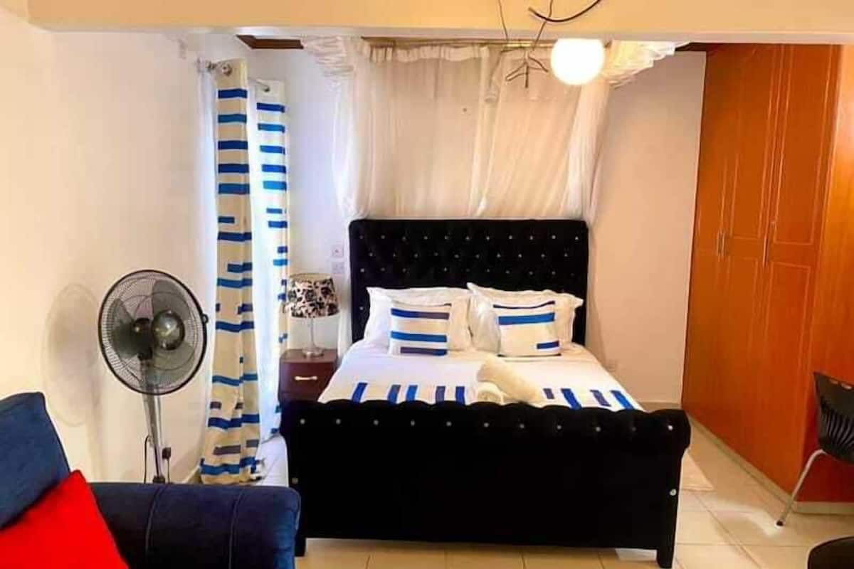 A bedroom with a bed, a fan, a nightstand, a lamp, and a wardrobe.