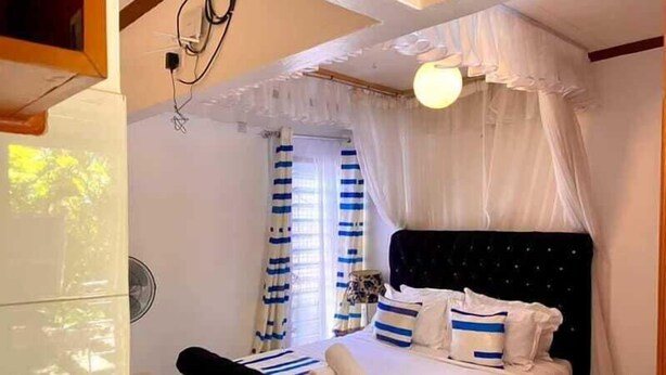 A bedroom with a bed, curtains, and a ceiling fan. - Kogelo Retreat Villas and Homes Kisumu (Kisumu)