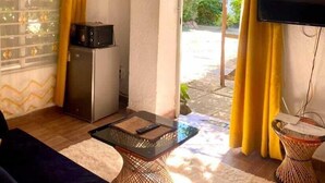 A living room with a sofa, a coffee table, a flat-screen TV mounted on the wall, and a small refrigerator. - Kogelo Retreat Villas and Homes Kisumu (Kisumu)