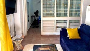 A living room with a blue sofa, a television, and a large window with blinds. - Kogelo Retreat Villas and Homes Kisumu (Kisumu)
