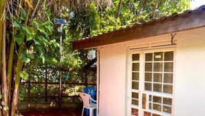 A small, single-story building with a white exterior and a red roof. There is a white door with a window, and a white chair is visible inside. - Kogelo Retreat Villas and Homes Kisumu (Kisumu)