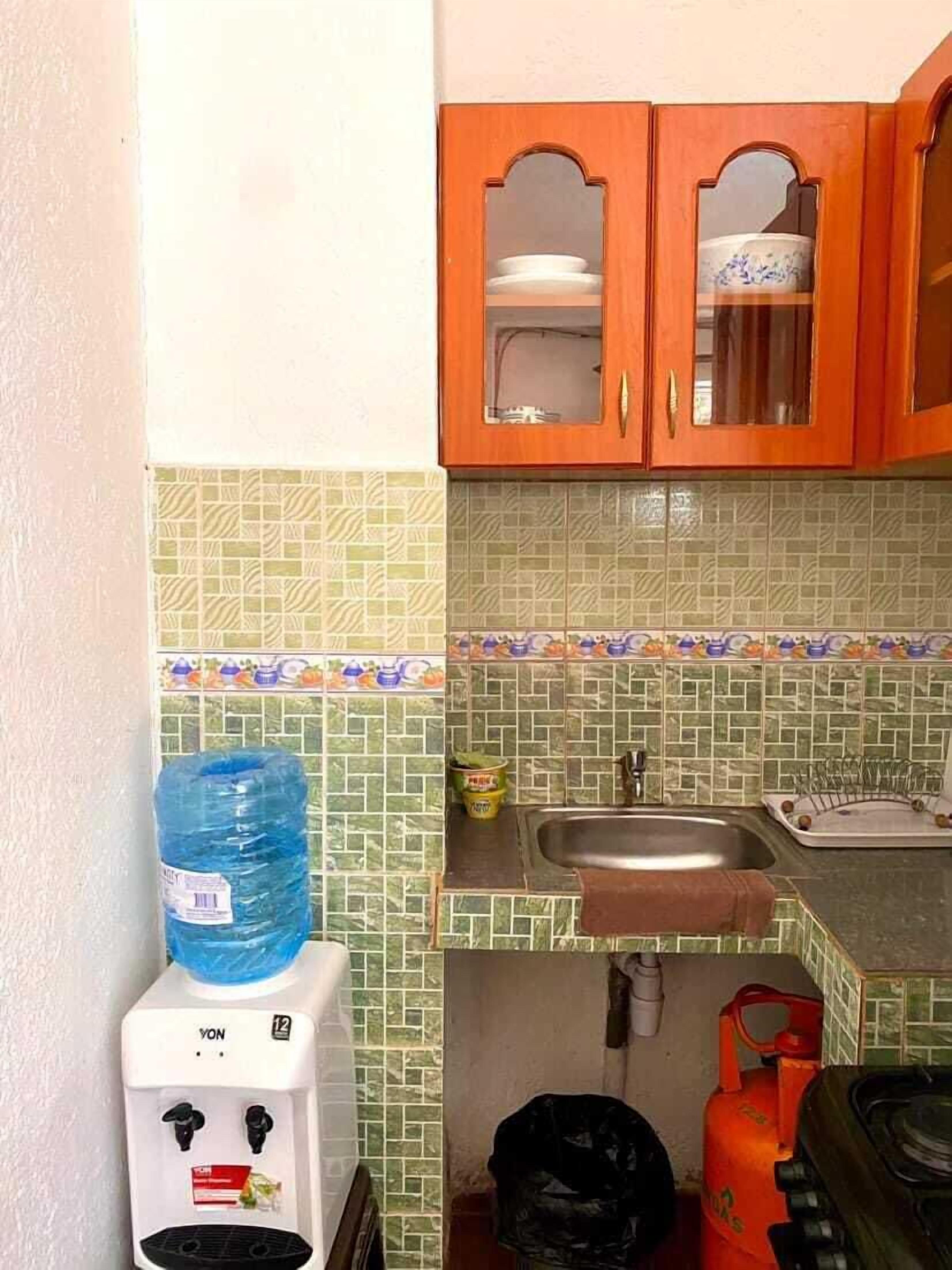 Una pequeña cocina con dispensador de agua, un lavamanos y una estufa a gas.