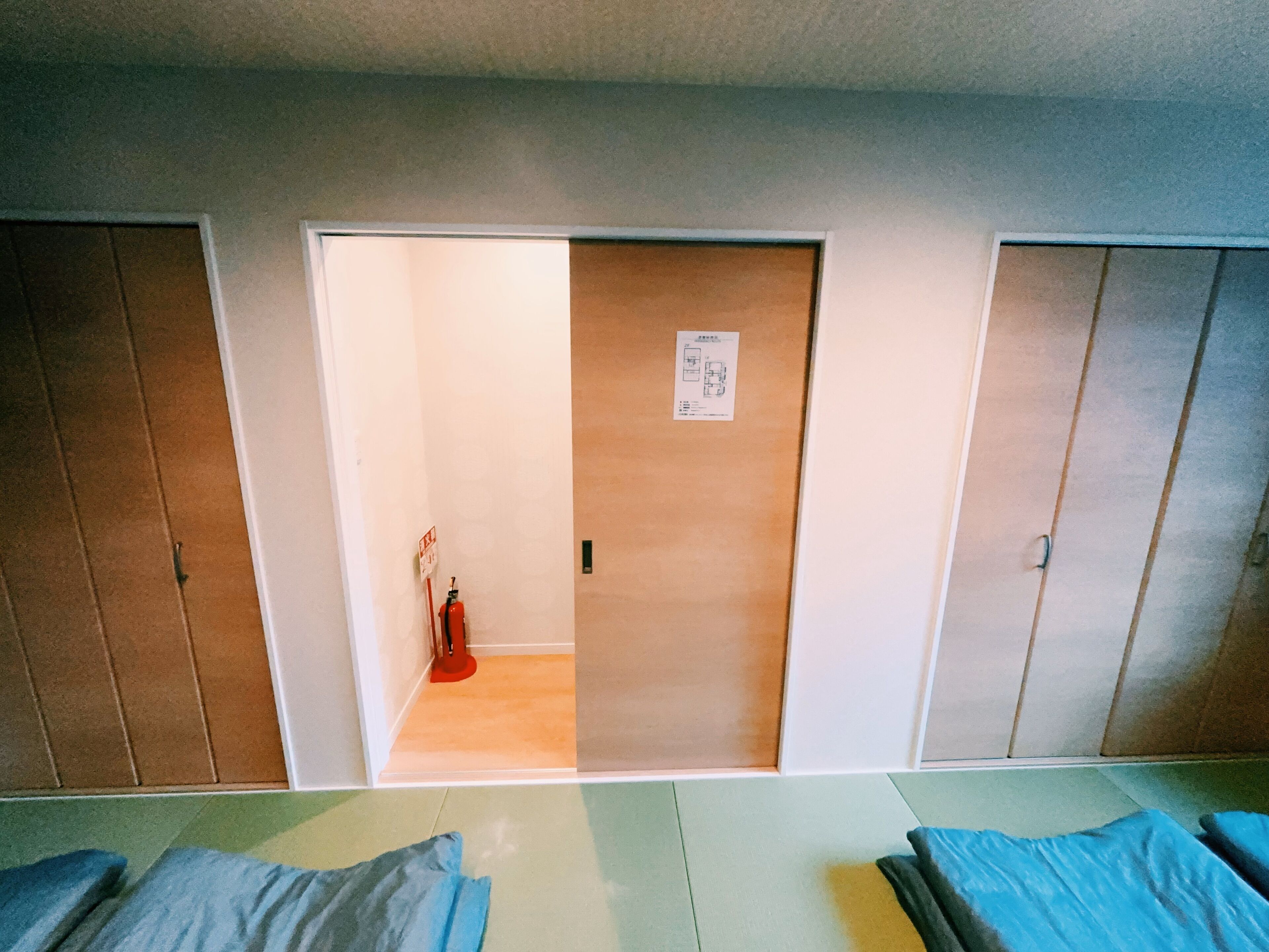 A room with a wooden door, a fire extinguisher, and a small sign on the wall.