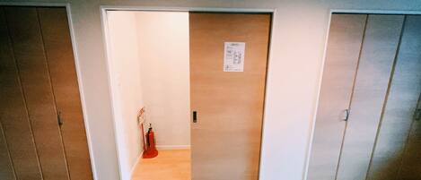A room with a wooden door, a fire extinguisher, and a small sign on the wall.