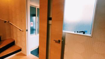 Een houten trap die leidt naar een kamer met een raam, een deur met een brievenluik en een luchtverkoeler aan de muur.