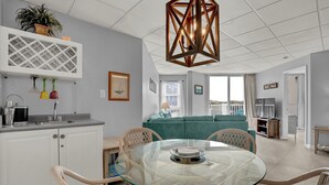 Una sala moderna con una mesa de comedor de vidrio, un sofá verde y una cocina con armarios blancos y un lavamanos.