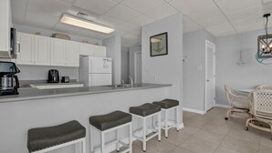 Una cocina moderna con armarios blancos, refrigerador empotrado, cafetera y una zona con taburetes de bar.