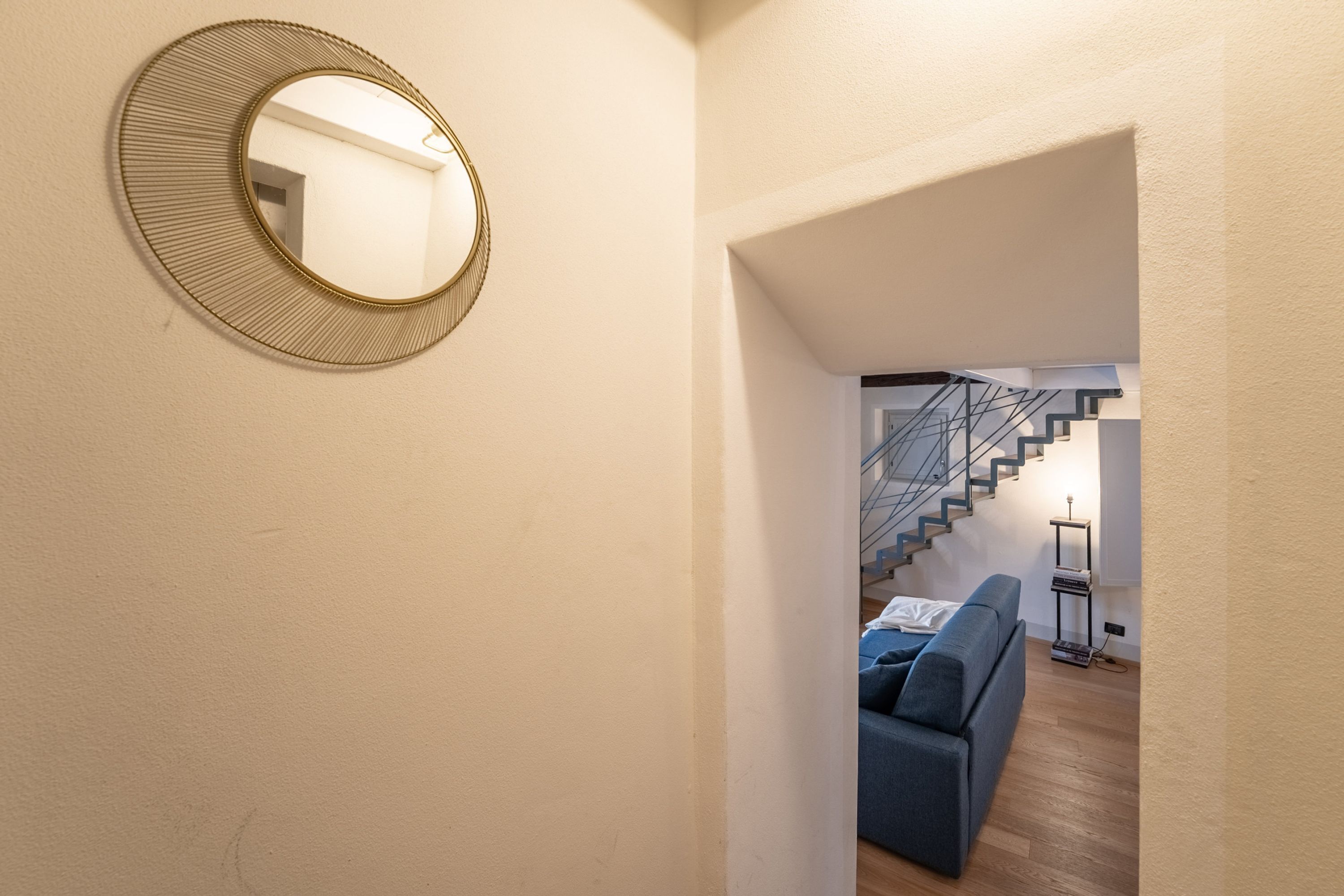 A hallway with a round mirror, a staircase, and a blue sofa.