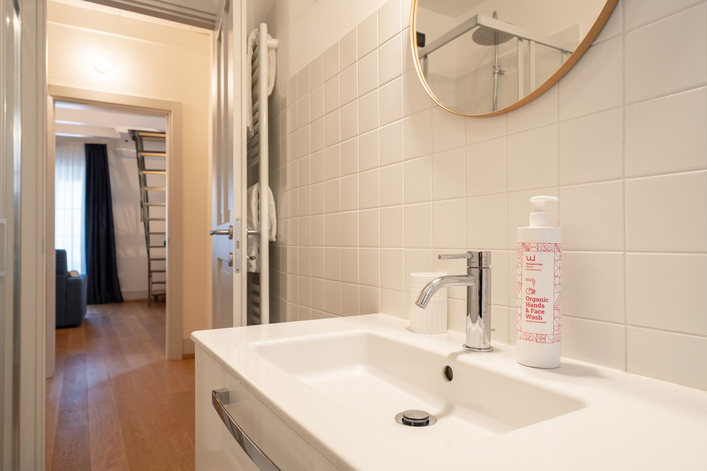 A bathroom with a white sink, a mirror, and a bottle of organic hand and face wash.