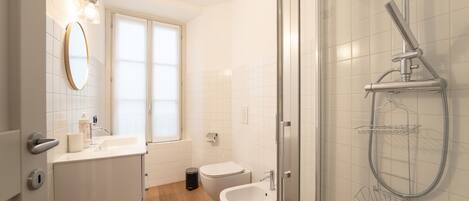 A modern bathroom with a glass shower enclosure, a white sink, and a bidet.