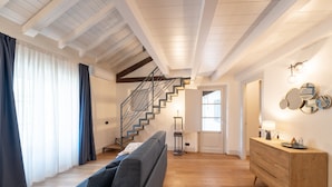 A modern living room with a staircase, wooden floors, a sofa, a dresser, and a wall with decorative mirrors. - Palazzo Odescalchi by Wonderful Italy - Apt 7 (Como)