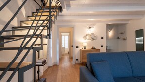 A modern living room with a blue sofa, wooden flooring, a staircase with metal railings, and a desk with a lamp. - Palazzo Odescalchi by Wonderful Italy - Apt 7 (Como)