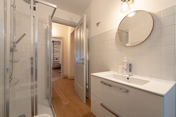 Un baño moderno con ducha envuelta en vidrio, un lavabo blanco con espejo y suelo de madera.