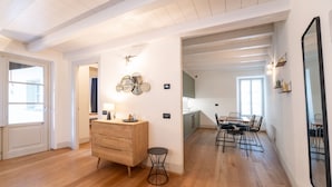 A spacious room with wooden flooring, a wooden dresser, a round black table, and a dining area with chairs. - Palazzo Odescalchi by Wonderful Italy - Apt 7 (Como)