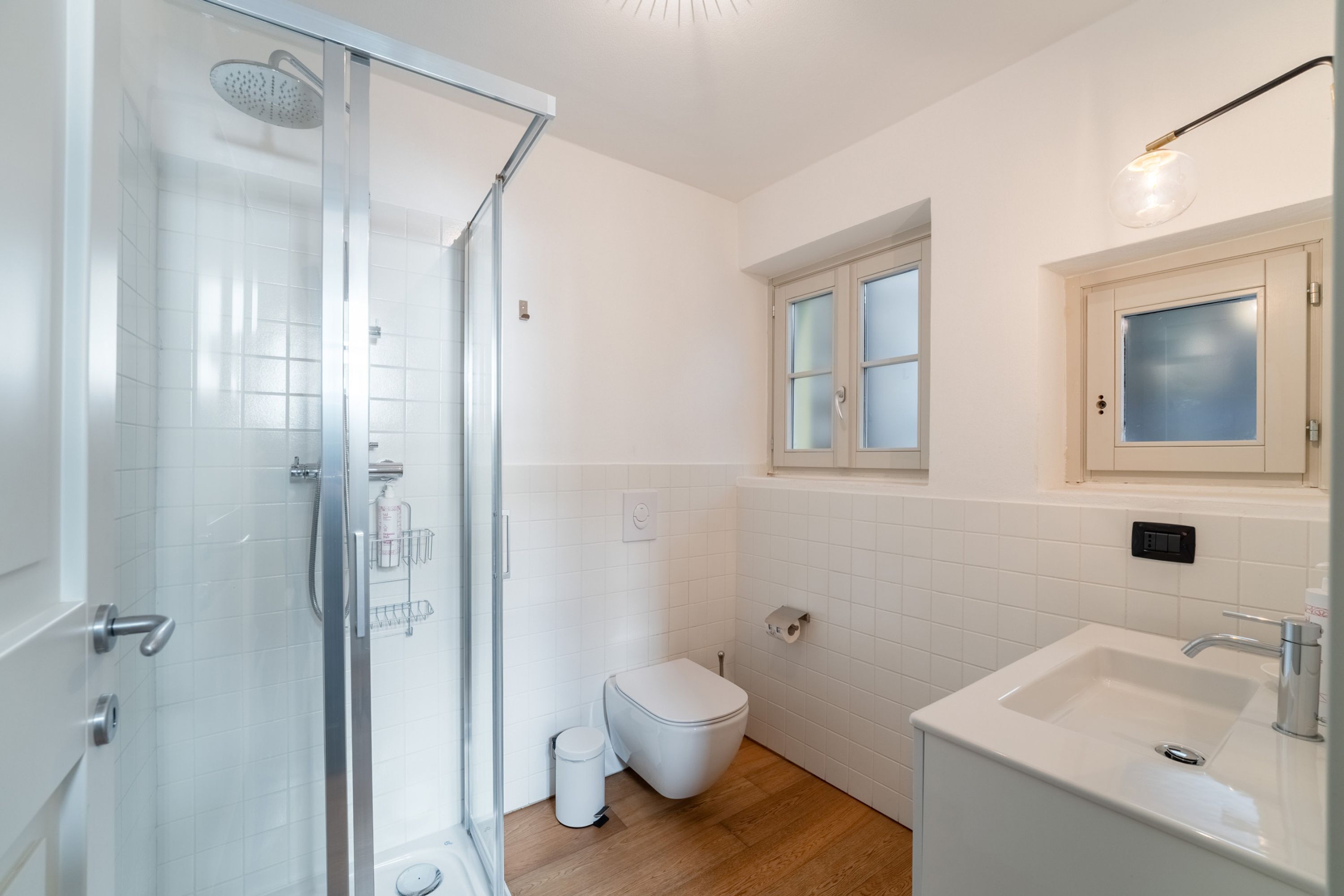 Un baño moderno con cabina de ducha de vidrio, inodoro, lavamanos y ventana.