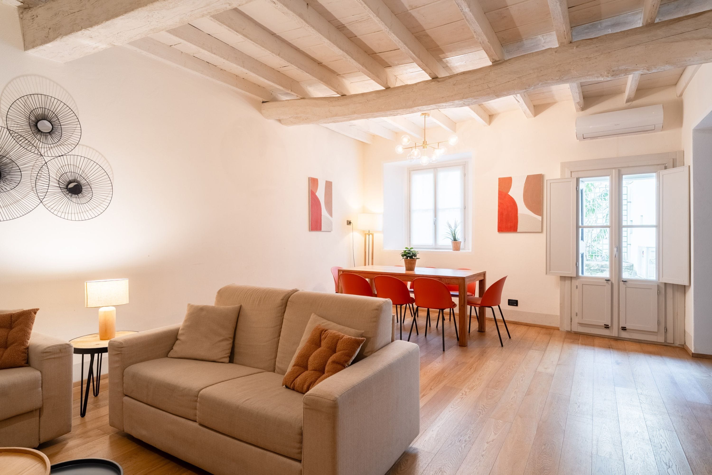 Un vaste espace de vie comprenant un canapé, une table à manger et des chaises. On y trouve une lampe sur une table d’appoint et des œuvres d’art accrochées aux murs.