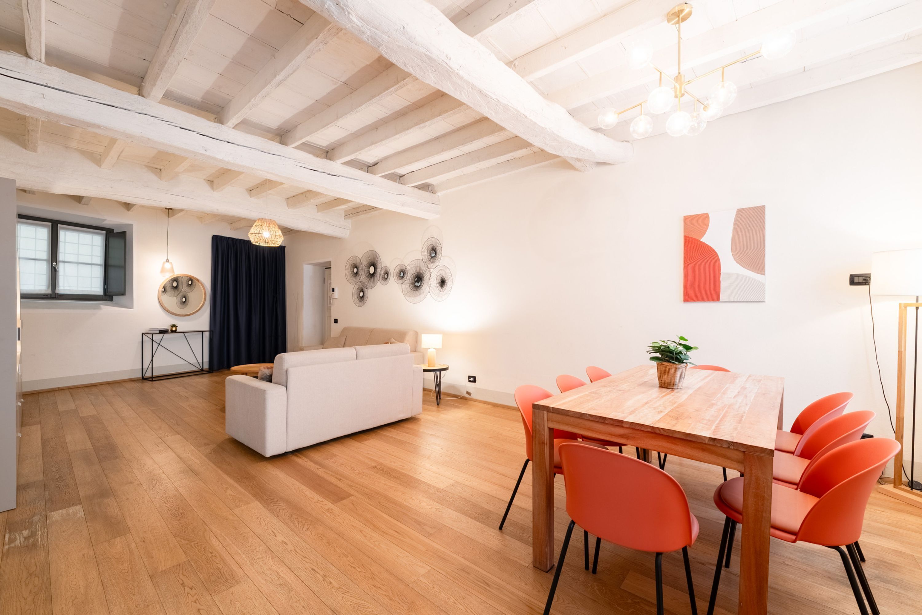 Ein modernes Wohnzimmer mit einem Holzesstisch, orangefarbenen Stühlen und einem weißen Sofa.