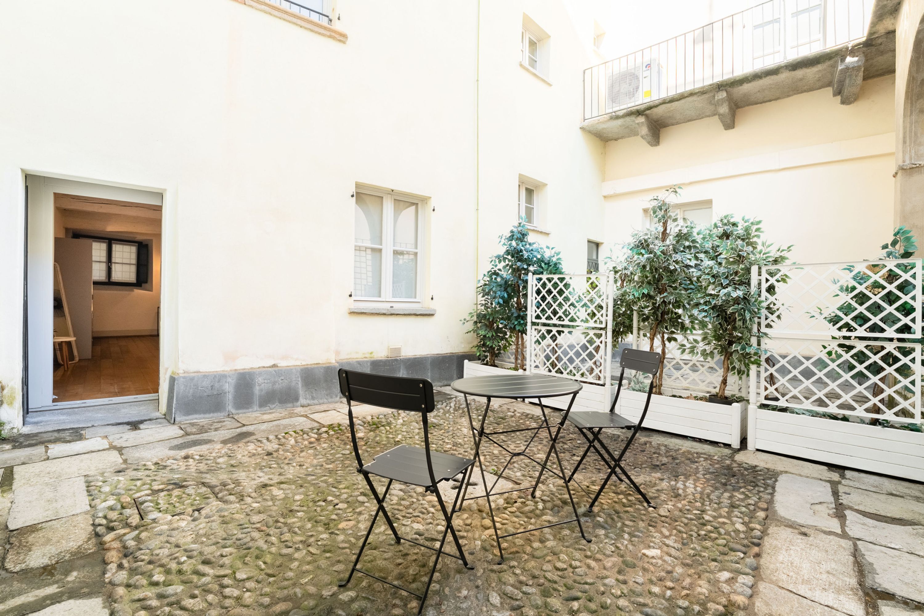 A courtyard with a stone floor, a small table, two chairs, and a white fence.
