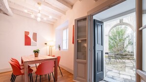 A dining area with a wooden table and red chairs, a lamp, and a view of an outdoor garden through an open door.