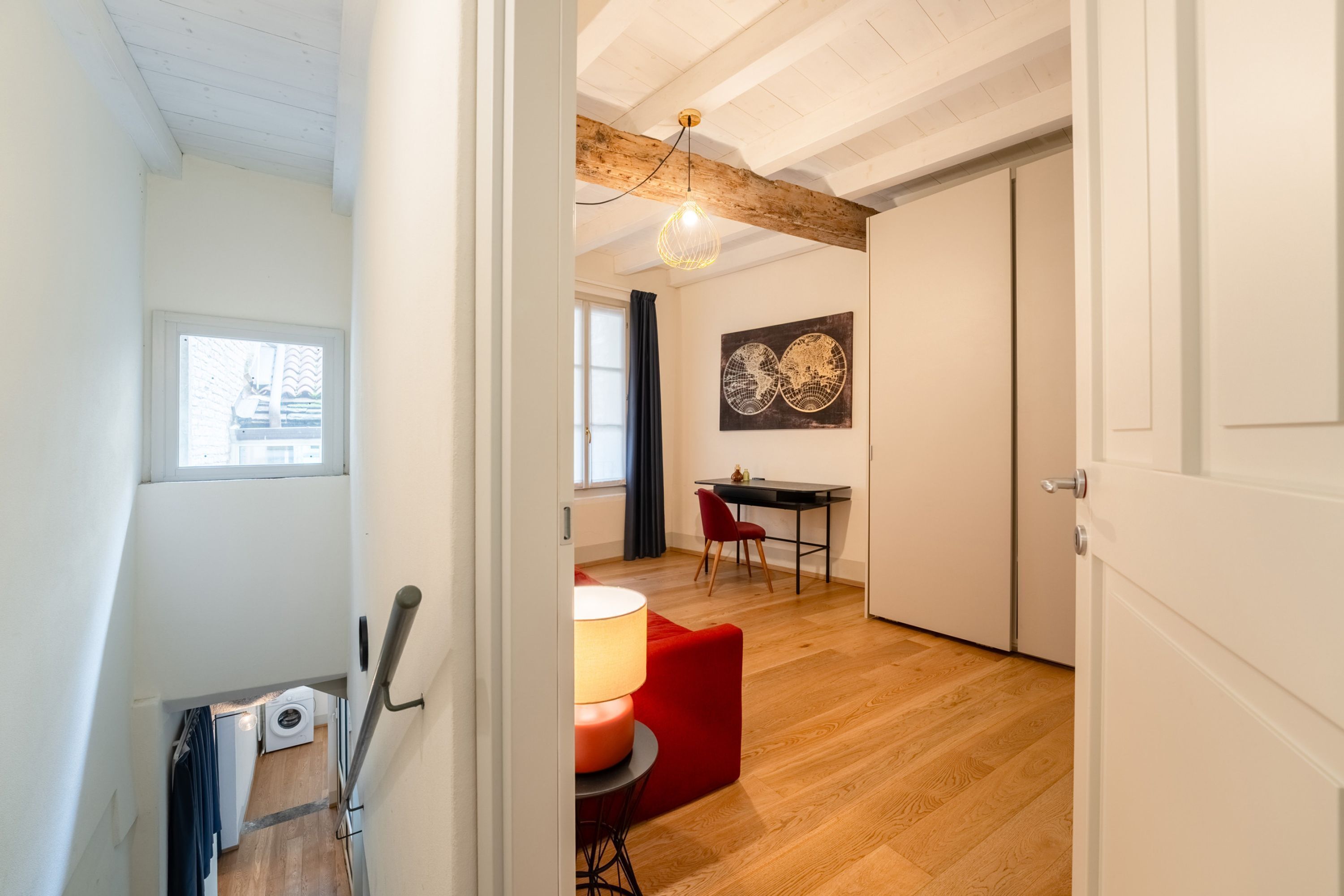 Un intérieur moderne avec un plafond en bois, un coin repas comprenant une chaise rouge, une table et une lampe.