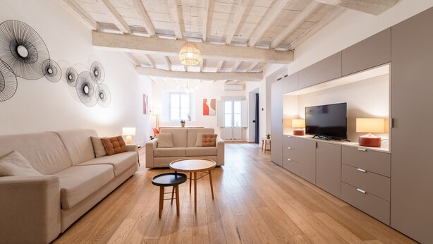 A spacious living room with a high ceiling, wooden beams, a large TV, and a sofa.
