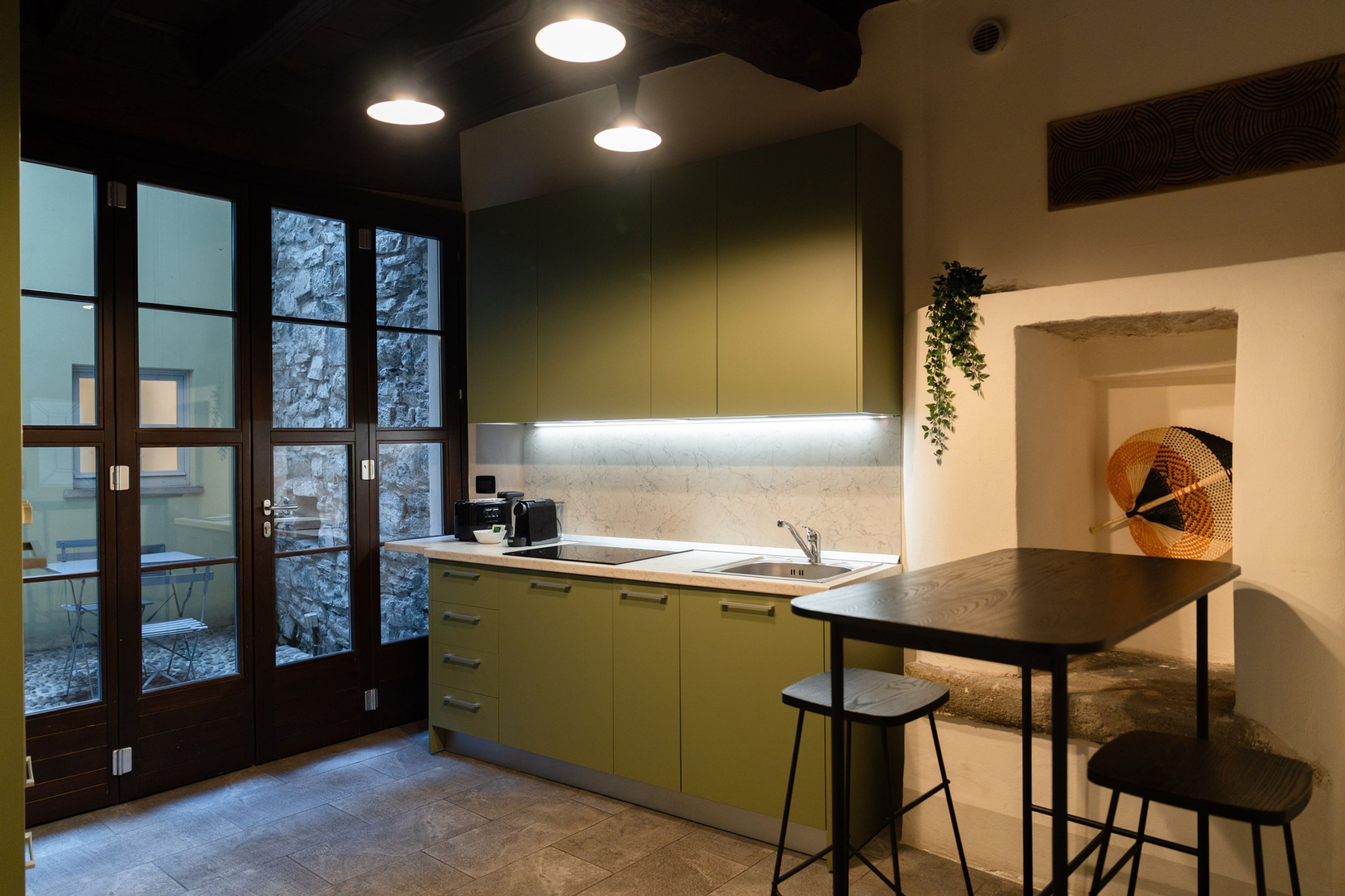Une cuisine moderne avec des meubles de couleur verte, un plan de travail noir et un tabouret de bar.