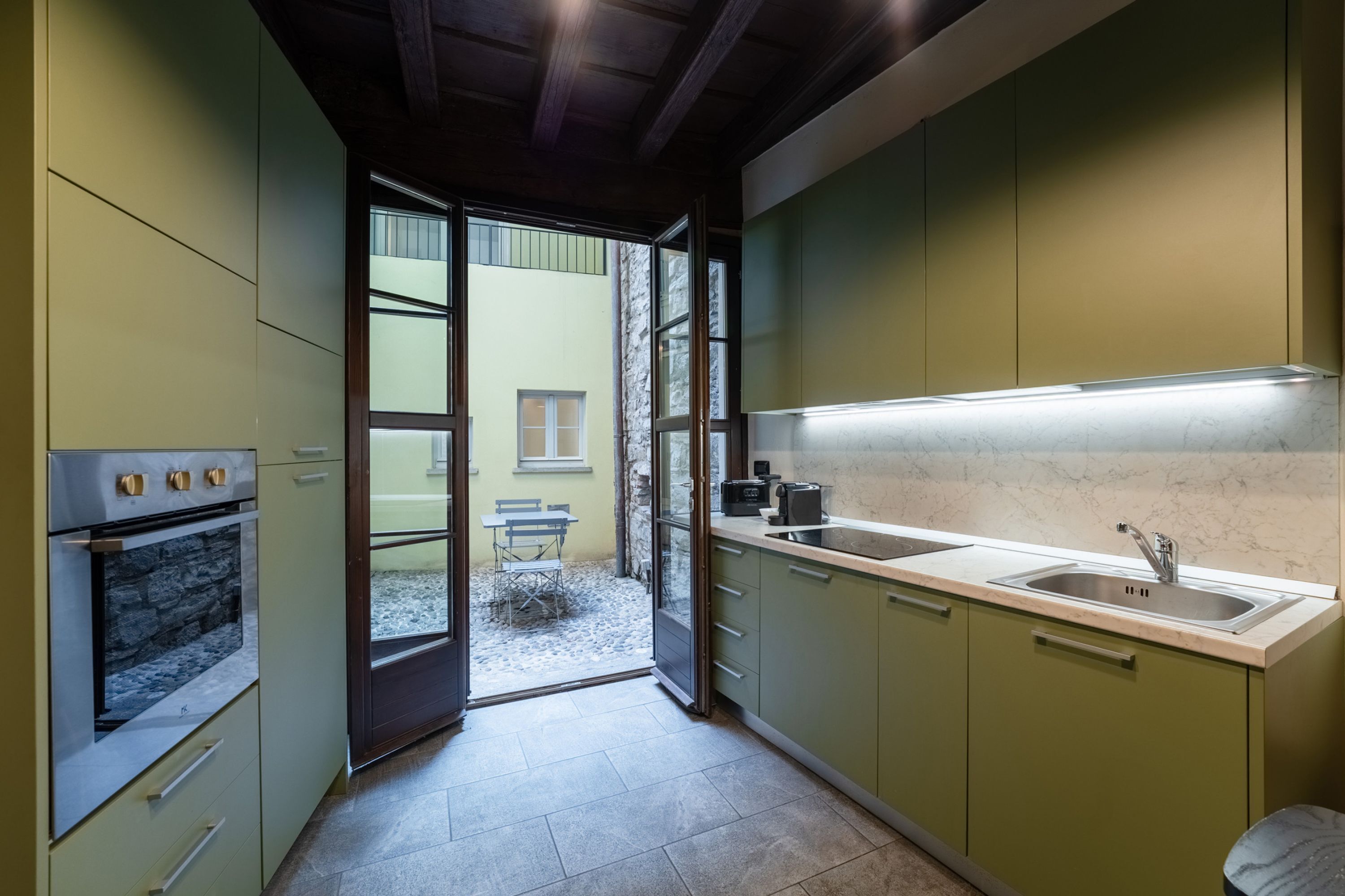 Eine moderne Küche mit grünen Schränken, einem eingebauten Ofen, einer Arbeitsplatte mit Spüle und Blick auf eine Terrassenfläche.