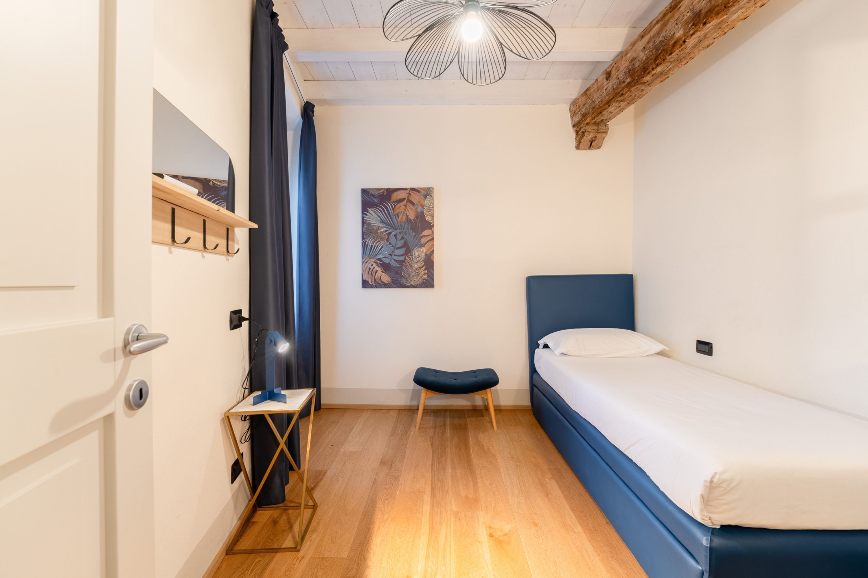 A small, well-lit room with a single bed, a desk, and a chair.