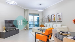 A modern living room with a sofa, a dining table, and a TV. There are potted plants and artwork on the walls. - Bloomfields 2BR Soul Beach in Saadiyat (Abu Dhabi)