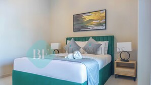 A neatly made bed with a green headboard, white bedding, and two pillows. There is a small bedside table with a lamp and a framed picture on the wall above the bed. - Bloomfields 2BR Soul Beach in Saadiyat (Abu Dhabi)