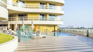 A modern hotel with a swimming pool, sun loungers, and a view of the city skyline. - Bloomfields 2BR Soul Beach in Saadiyat (Abu Dhabi)