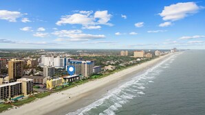 Un paisaje urbano costero con un hotel frente a la playa que tiene varios pisos, una piscina y vistas al océano.