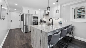 A modern kitchen with a marble island, stainless steel appliances, and pendant lighting. - Modern Escape - Oceanfront, Family-Friendly Condo, Luxe Kitchen + Pool, Sleeps 6 (Myrtle Beach)