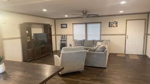 A spacious living room with a dark wood floor, a large flat-screen TV, a dark wooden entertainment center, two gray sofas, and a ceiling fan. - Mountain Top Retreat with ATV Route Access (LaFollette)
