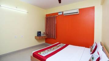 Una habitación de hotel con cama, aire acondicionado, ventilador de techo y un pequeño estante con artículos de aseo.