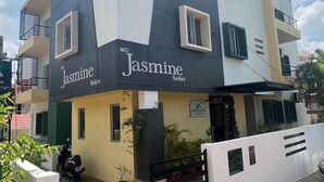Een modern gebouw met het bordje 'Jasmine Suites'. Het heeft meerdere verdiepingen, balkons en een hekwerk.