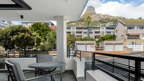 A balcony with a table and chairs, overlooking a residential area with buildings and a mountain. - Central Minimalist 1bed by the Ocean The Bantry (Cape Town)