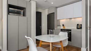 A compact kitchen with a microwave, refrigerator, and a small dining area with a table and chairs. - Central Minimalist 1bed by the Ocean The Bantry (Cape Town)