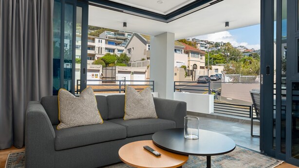 A modern living room with a grey sofa, a round coffee table, and a balcony with a view of the city. - Central Minimalist 1bed by the Ocean The Bantry (Cape Town)