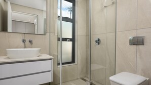 A modern bathroom with a glass shower enclosure, a white sink, and a toilet. - Central Minimalist 1bed by the Ocean The Bantry (Cape Town)
