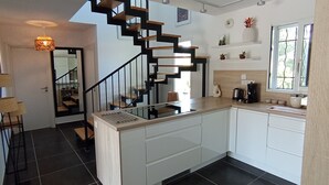 Une cuisine moderne dotée d’un îlot central, d’un escalier avec des marches en bois et d’une fenêtre donnant sur un paysage verdoyant.